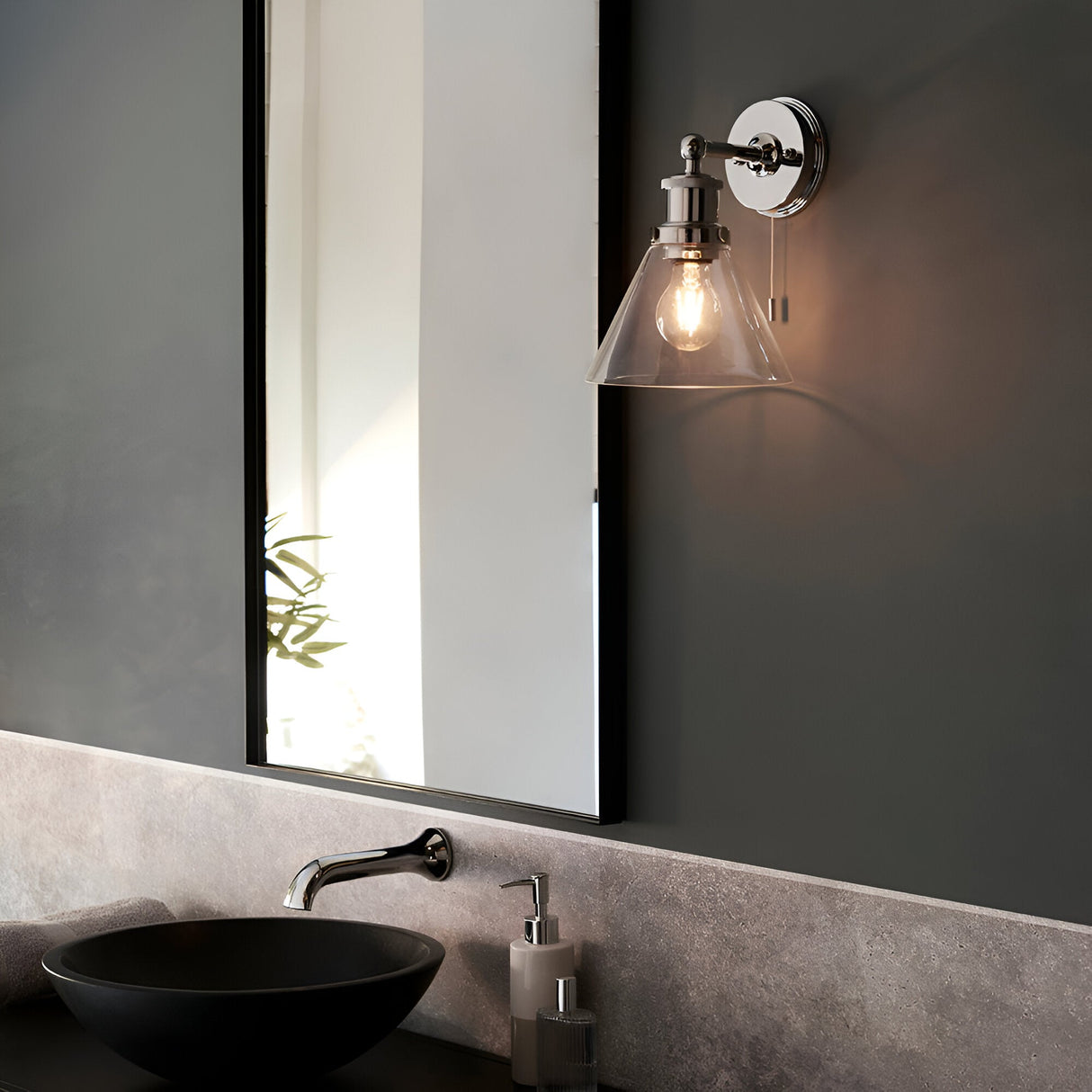Endon Cranmore bathroom wall light in polished chrome with a cone-shaped clear glass shade and pull switch, mounted beside a mirror above a stone basin.