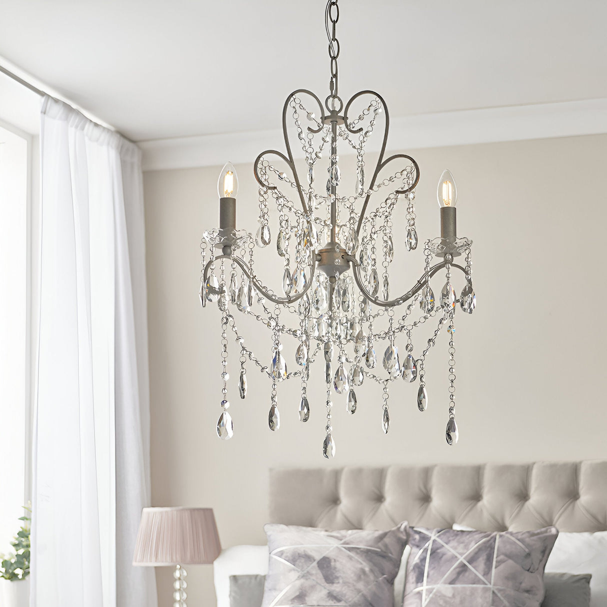Endon Aldwood 3 light pendant in aged silver with faceted crystal drops and swags, hanging above a tufted bed in a soft neutral bedroom.
