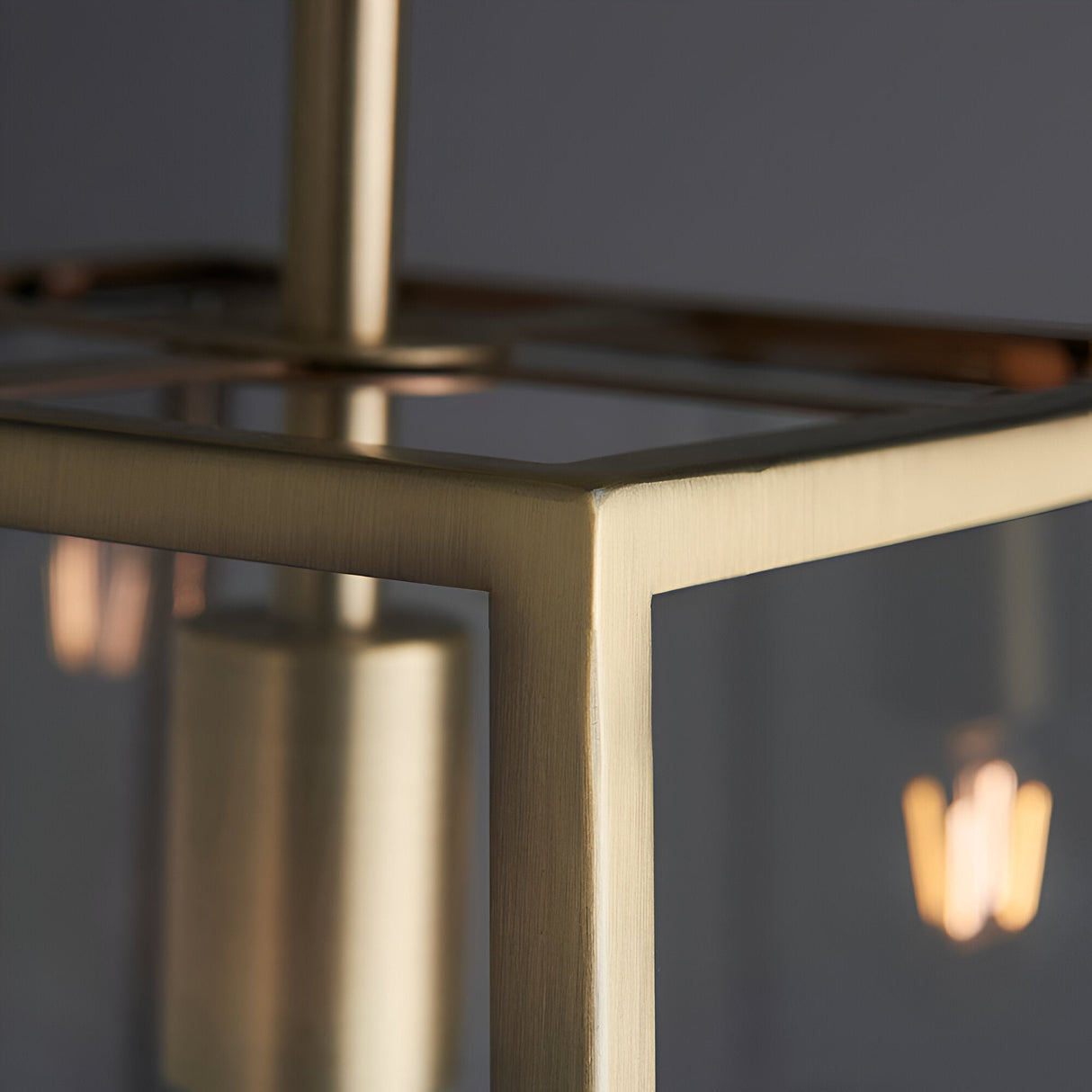 Close-up of Endon Brenton lantern pendant showing brushed brass tapered frame corner, clear glass panels and a warm filament E27 bulb glowing within.