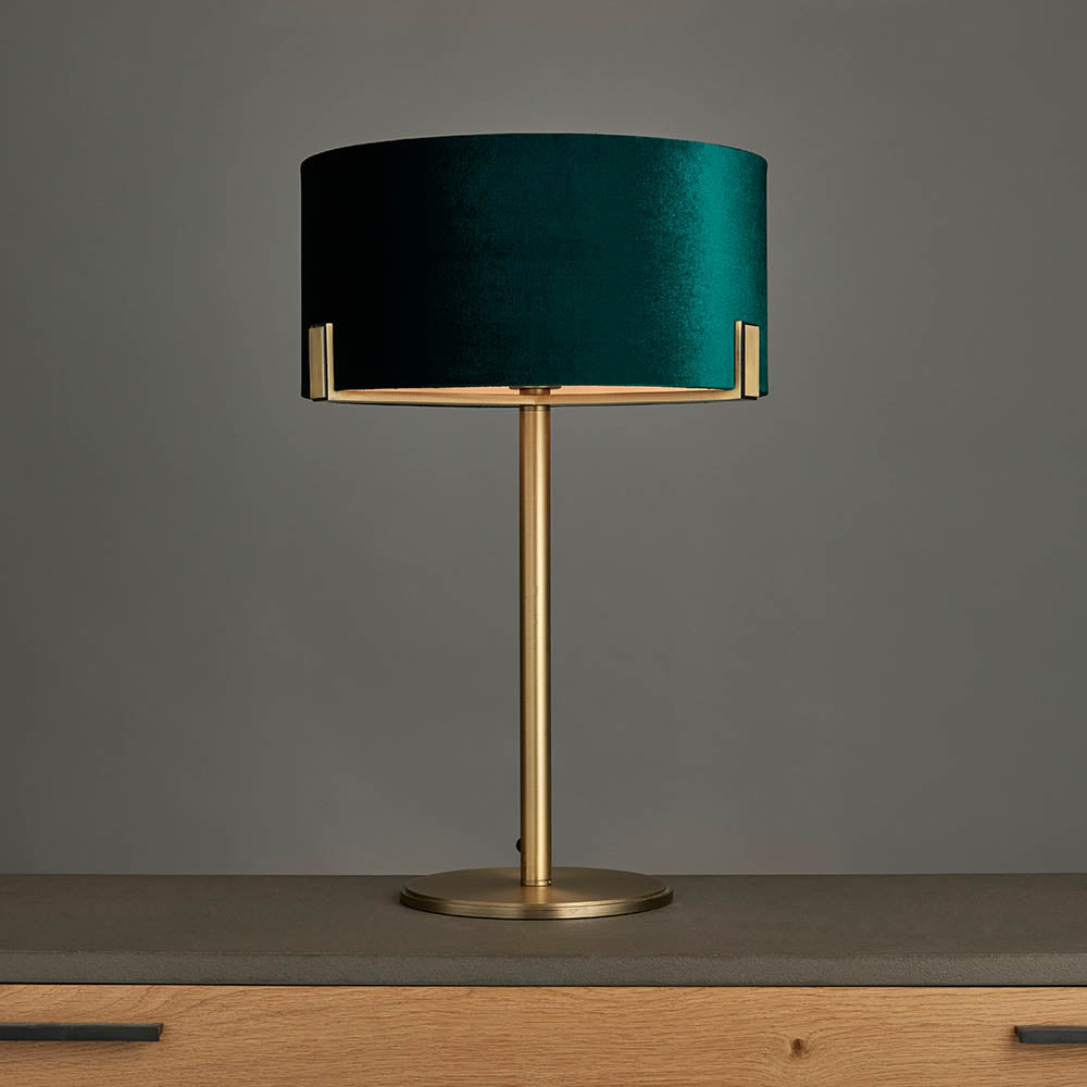 Brendon Table Lamp with a drum-shaped green velvet shade on a slim matt antique brass base, set against a plain grey background.
