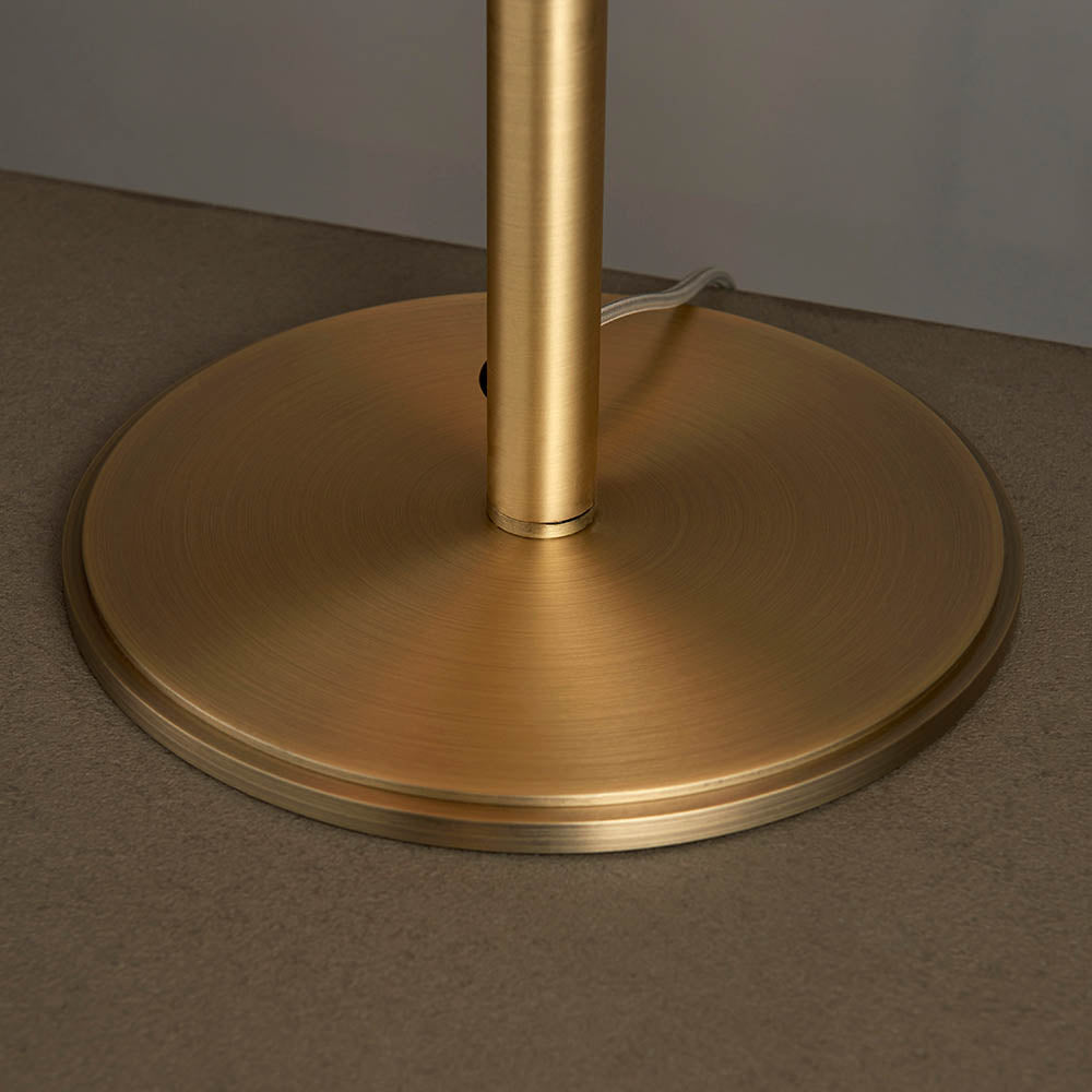 Close-up of the Brendon Table Lamp's round, matt antique brass base and stem, showing brushed metal texture on a light surface.