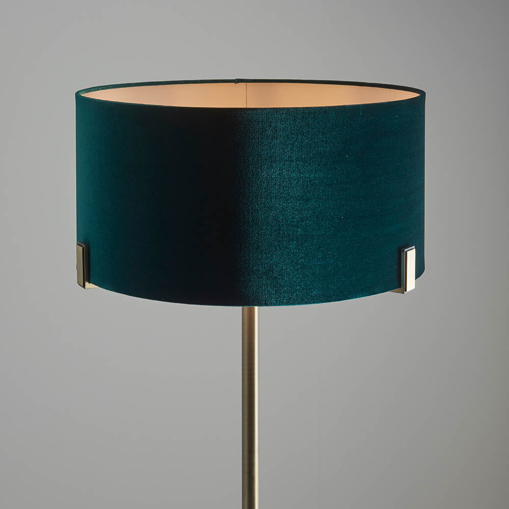 Endon Brendon floor lamp with a green velvet cylinder shade held on slim antique brass metalwork, shown against a plain grey background.