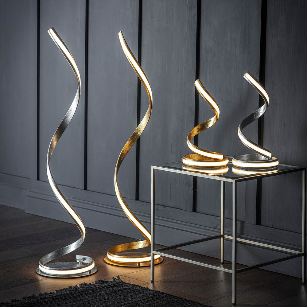 Endon Neve floor and table LED lamps with spiralling silver leaf curves and white diffusers, displayed beside a glass side table against grey panelling.