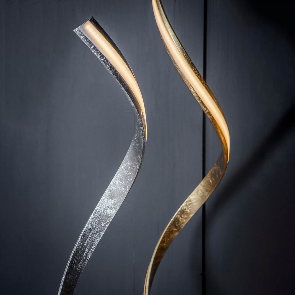 Endon Neve LED floor lamps with flowing illuminated curves in silver leaf and gold finishes, shown against a dark grey backdrop.