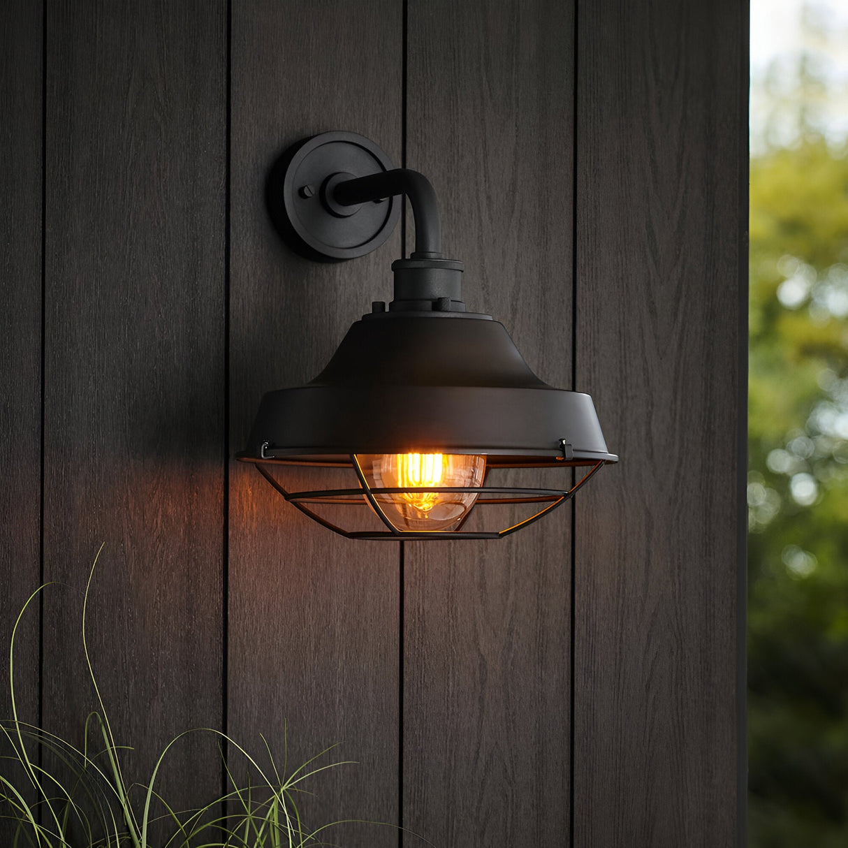 Caldton Outdoor Wall Light in matt black, industrial style with wire cage over glass shade and lit filament bulb, mounted on wooden panelled wall.