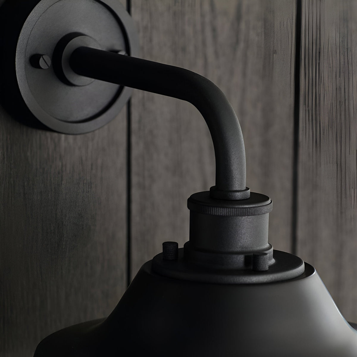 Close-up of the Caldton Outdoor Wall Light in matt black, showing the curved arm, knurled fitting, and shade top against a wood-panelled wall.
