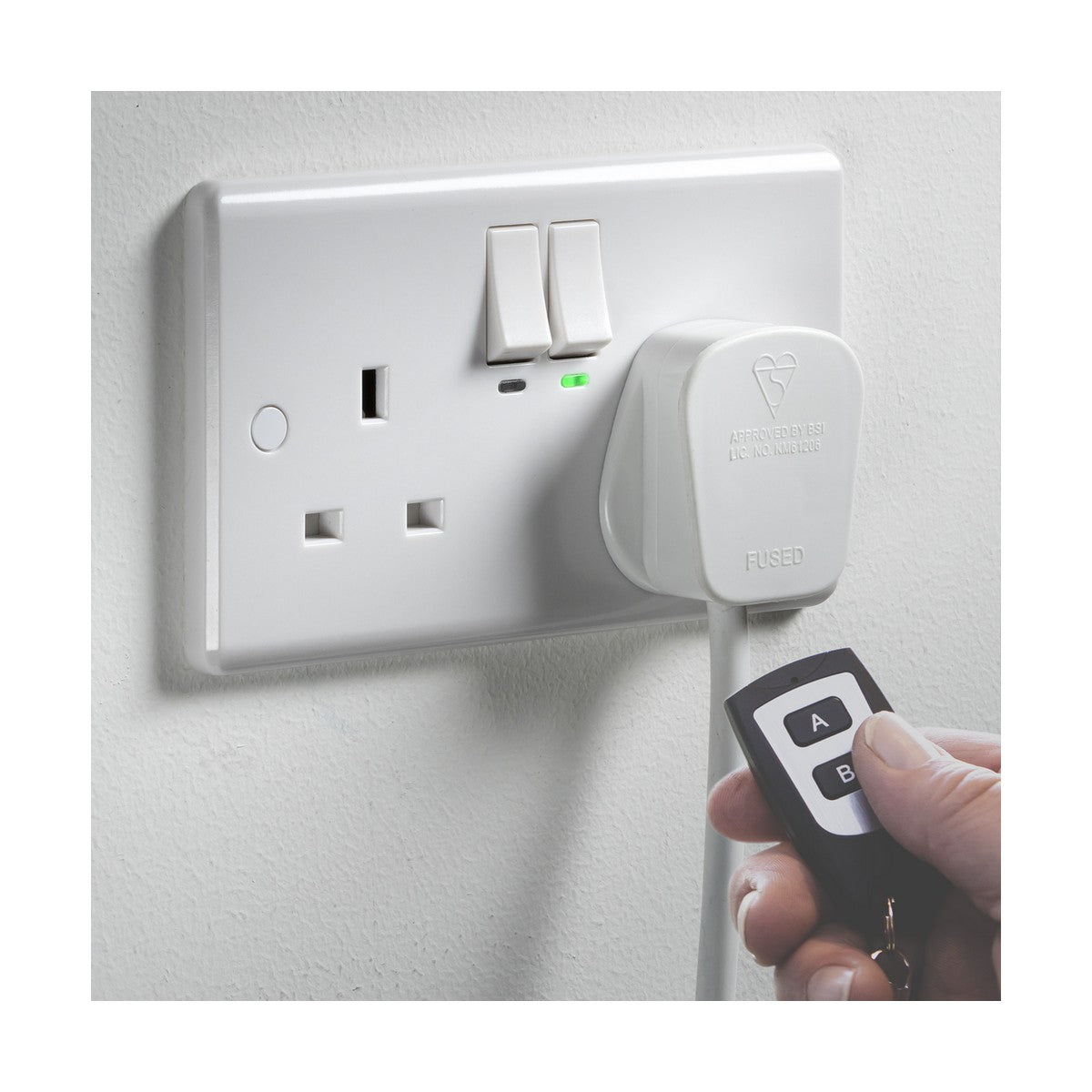 A UK electrical wall socket, identified as the 13A 2 Gang SP Switched Socket With RF Remote Control, includes two outlets and switches, with a plug connected to one of the outlets. A hand holds a key fob remote nearby with buttons labeled A and B. The green light on the 230V remote control socket is lit, indicating it is currently in use.
