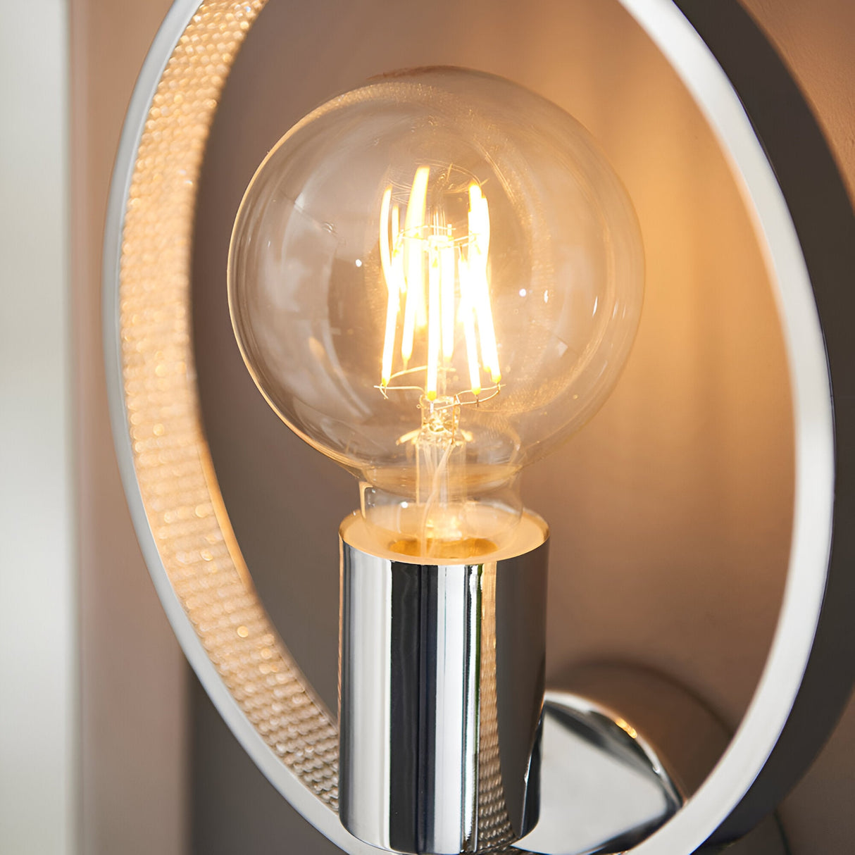 Close-up of Endon Carlcombe bathroom wall light showing chrome ring with faceted detail, central E27 globe filament bulb lit warm.