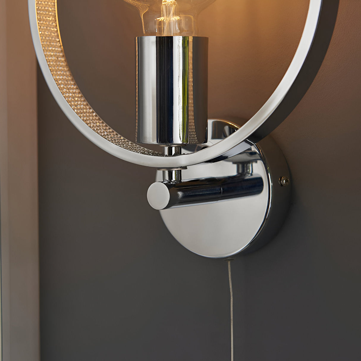 Close-up of Endon Carlcombe chrome bathroom wall light showing the polished circular backplate, pull cord switch, E27 lamp holder and faceted ring detail.
