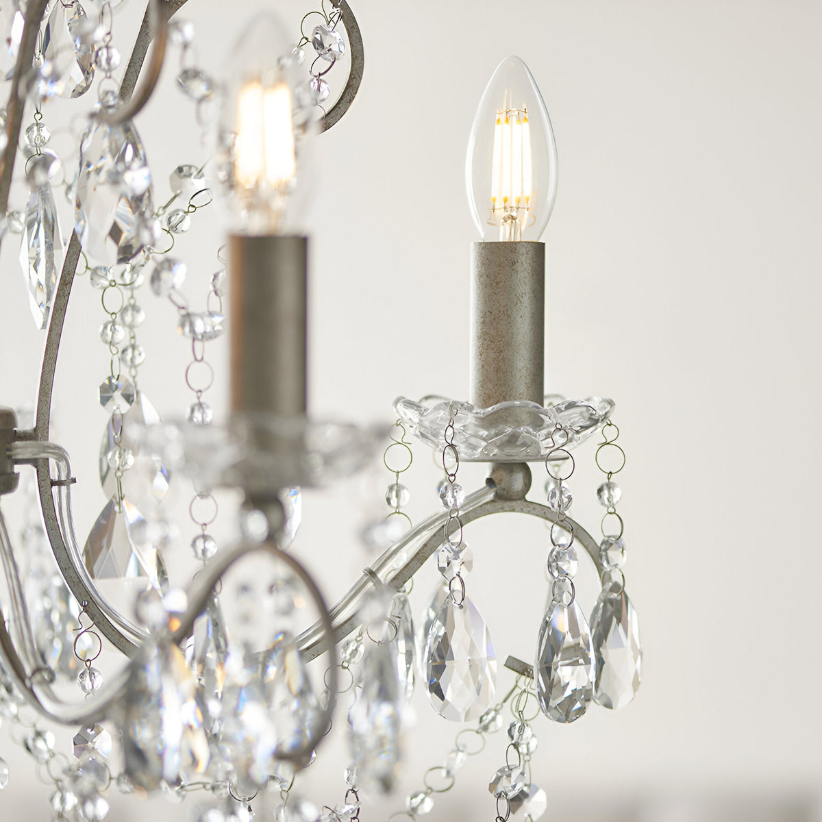 Close-up of Endon Aldwood 5 light pendant showing aged silver arms, cut crystal droplets, glass bobeches and lit E14 candle bulbs.