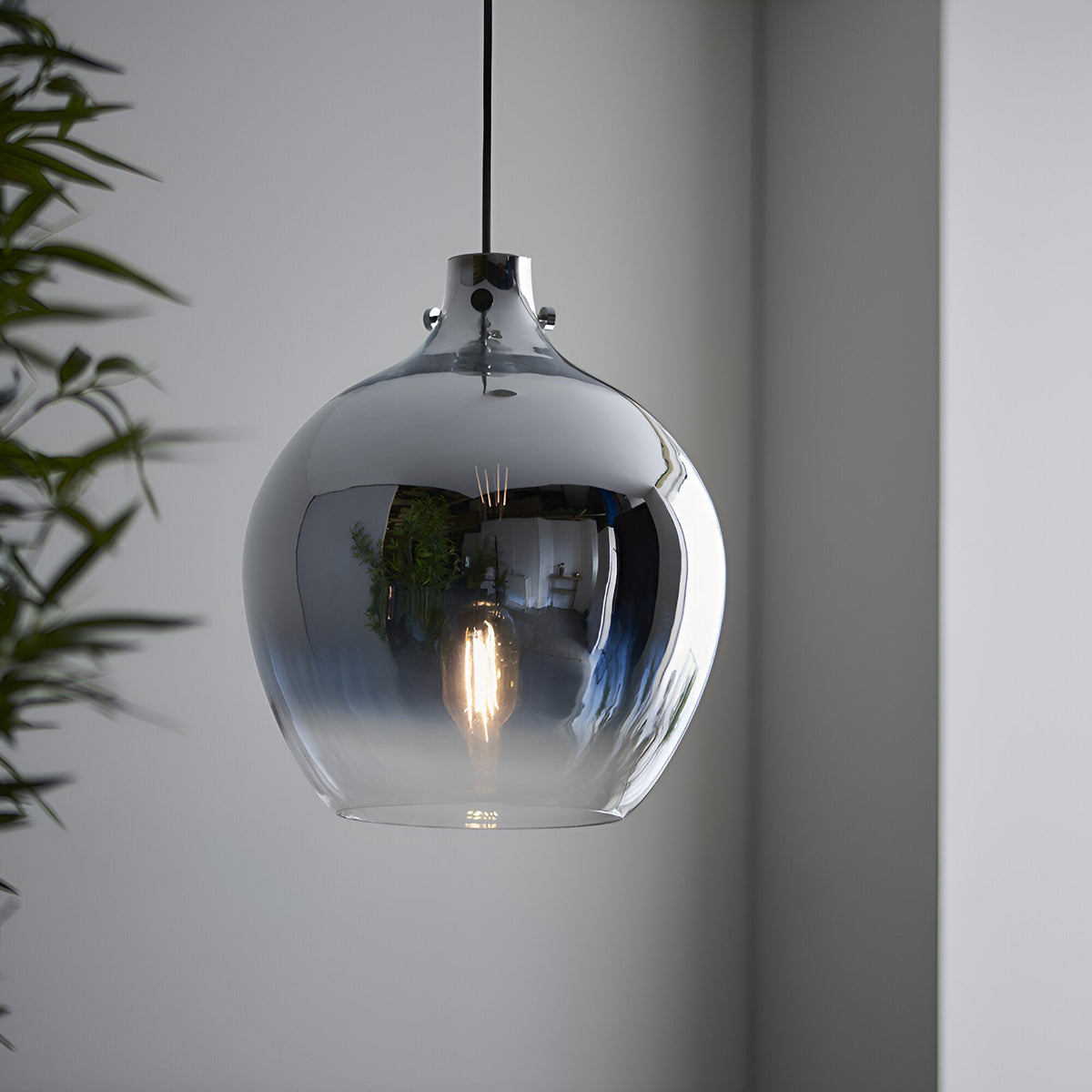 Castworth Glass Pendant in chrome, single-drop globe shade with ombre mirrored finish and visible E27 bulb, hung in a room with a green plant nearby.