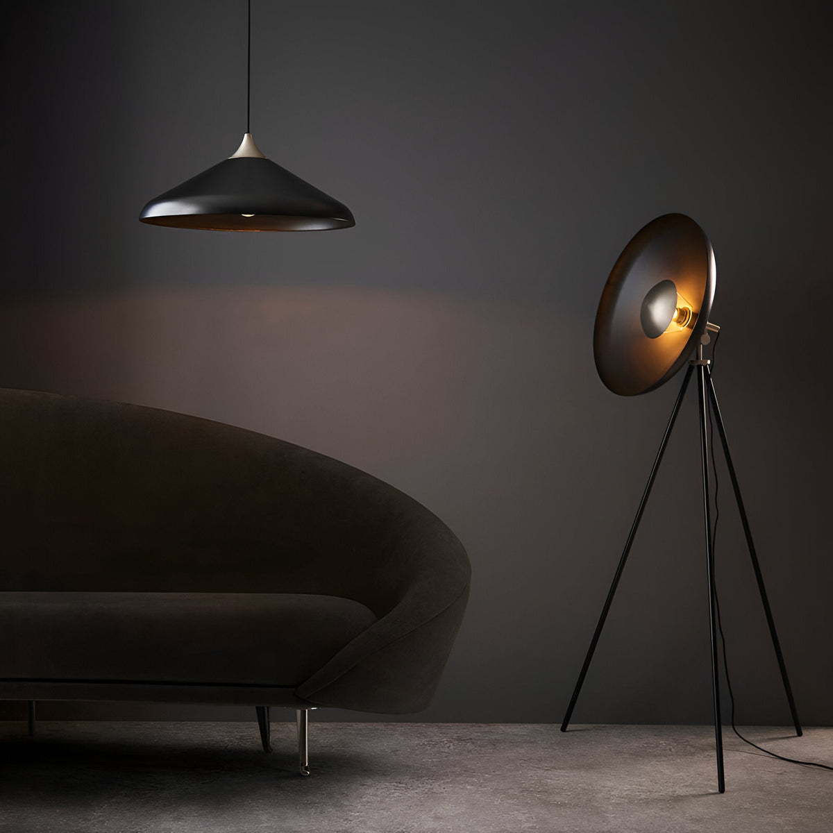 Endon Bramshaw tripod floor lamp in matt black with large tilted dish shade, styled beside a curved sofa and pendant light in a dim living room.