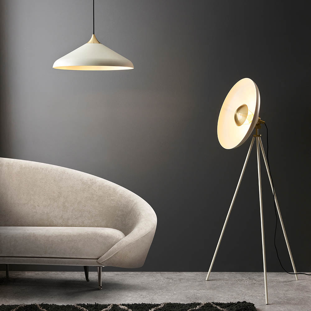 Endon Bramshaw floor lamp in white with brushed brass details, angled disc shade on a tripod stand, beside a cream curved sofa and pendant light.