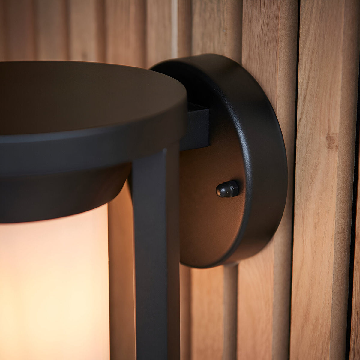 Close-up of Endon Ashdale outdoor wall light showing textured black aluminium bracket and white polycarbonate shade mounted on a wooden slatted wall.