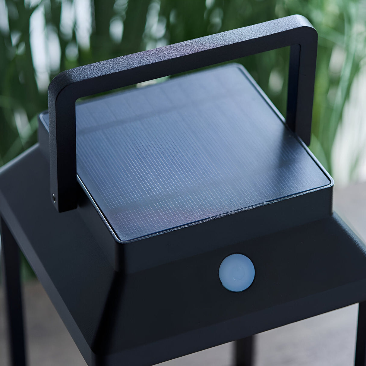 Caldshaw LED Solar Table Lamp in black with square solar panel top, carry handle, and touch dimmer button, shown outdoors near greenery.