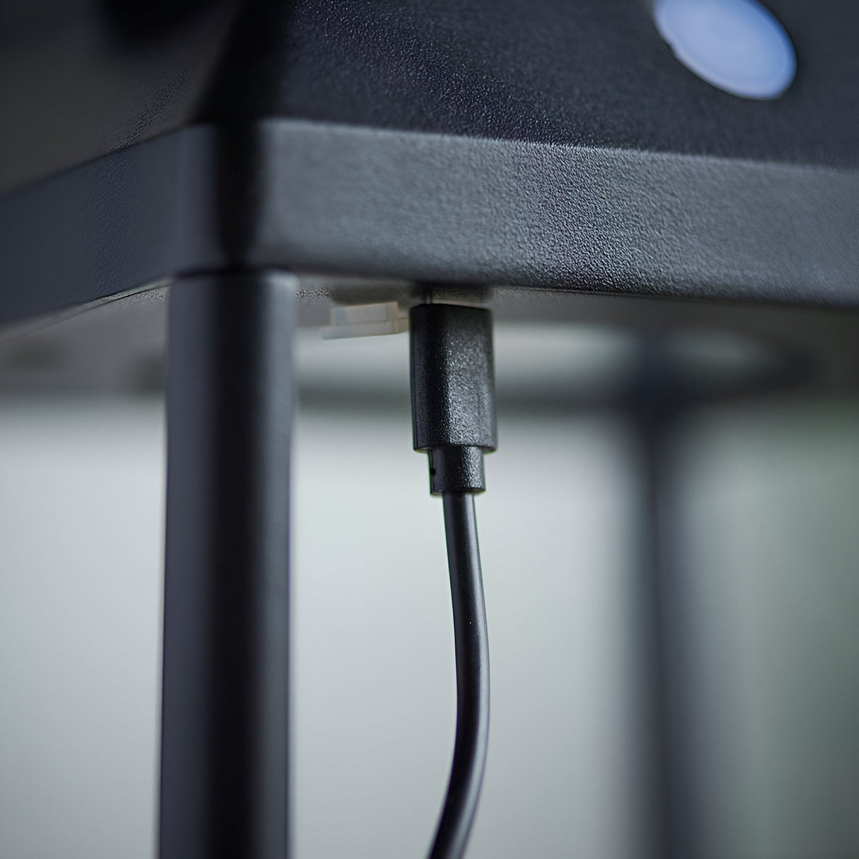 Close-up of the Caldshaw LED Solar Table Lamp in black showing the USB charging port and cable beneath the textured metal base.