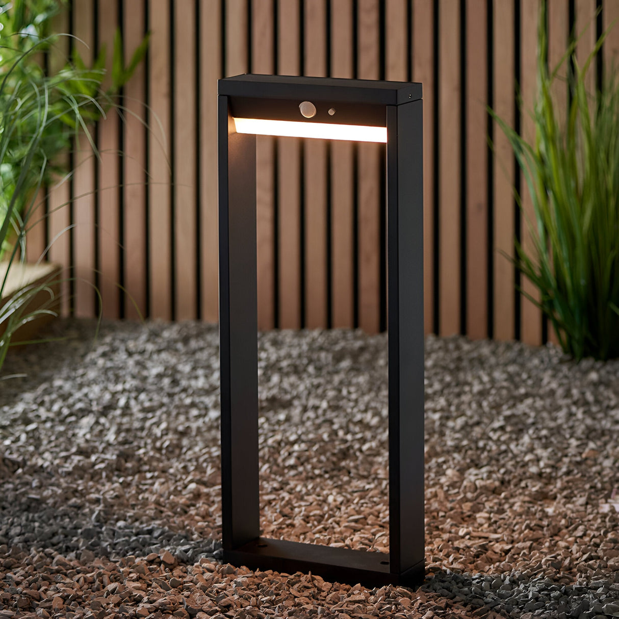 Endon Blythe LED solar post light in matte black aluminium with warm white diffuser and PIR sensor, on gravel beside a slatted wood fence and grasses.