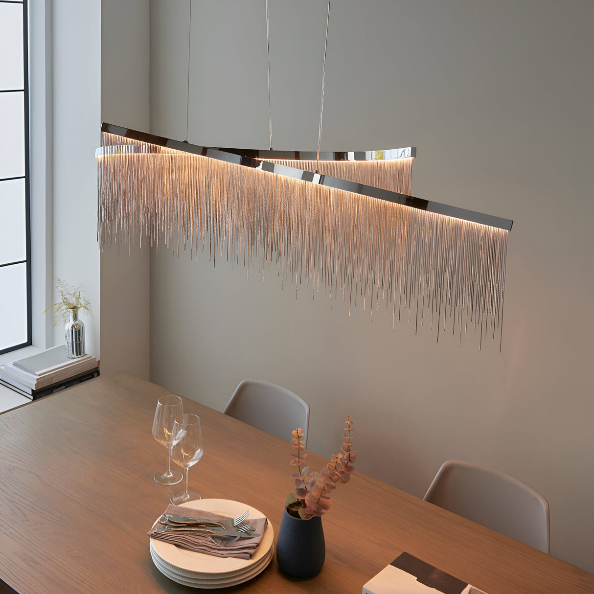 Endon Caststead linear pendant in polished chrome with cascading silver chain fringe, suspended above a wooden dining table in a modern room.