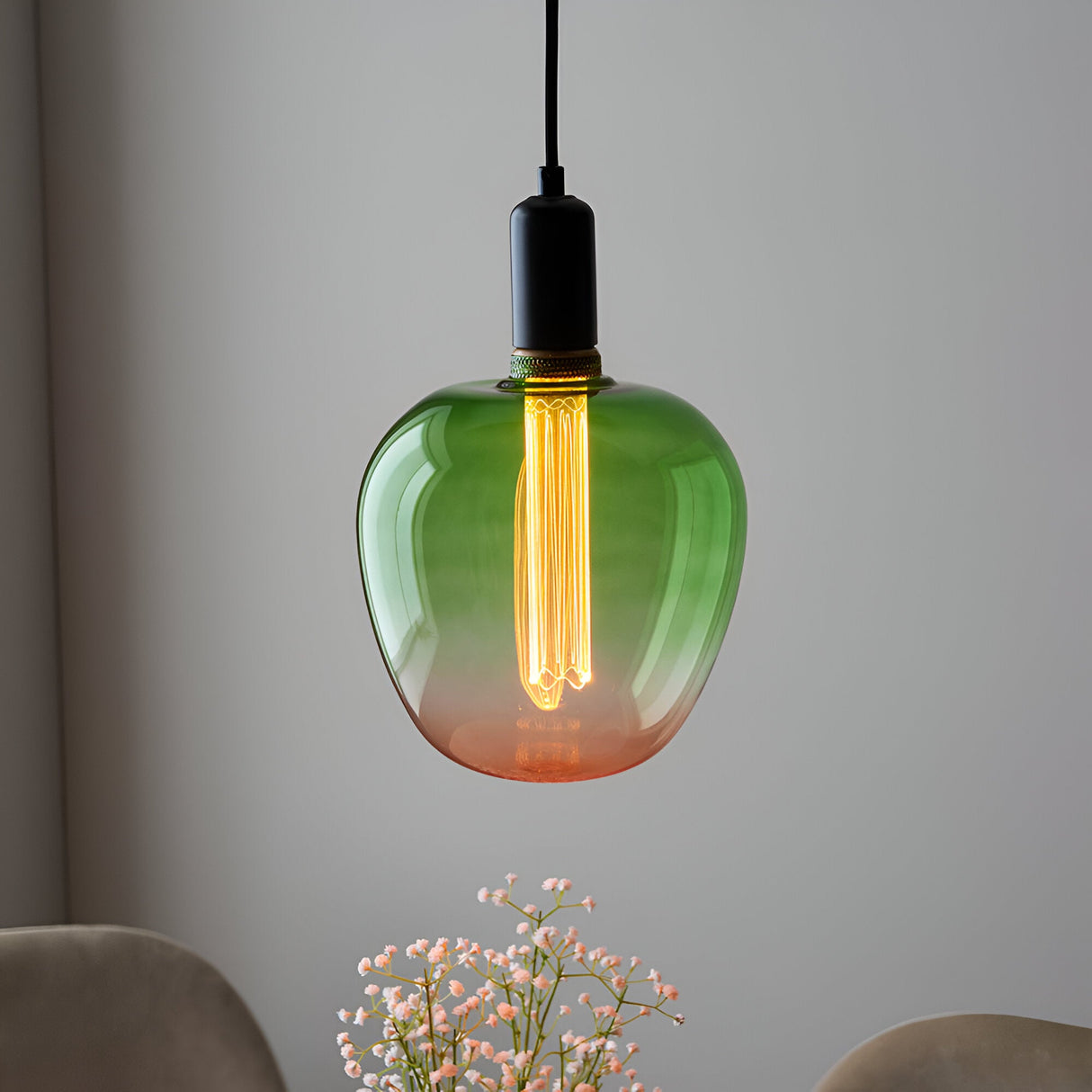 Endon 2.8W E27 LED filament bulb with green-to-pink ombre glass, glowing warm white in a black pendant fitting above pale flowers.