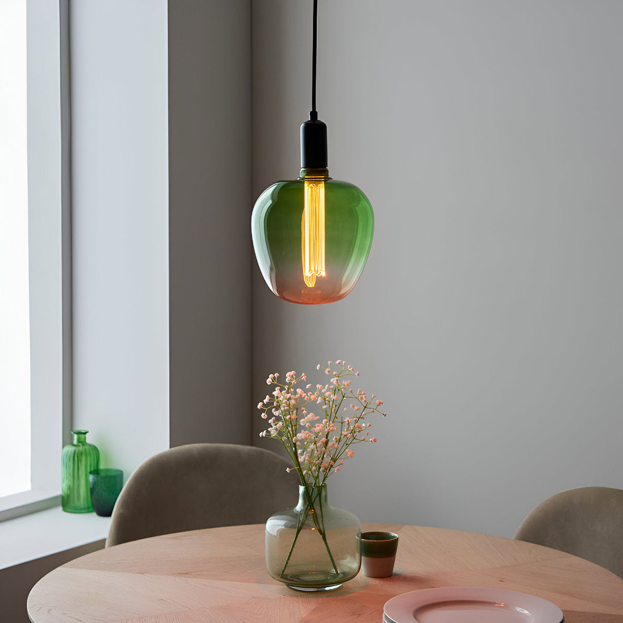Endon 2.8W E27 LED filament bulb with green-to-pink ombre glass, glowing warm white above a wooden dining table with flowers by a window.
