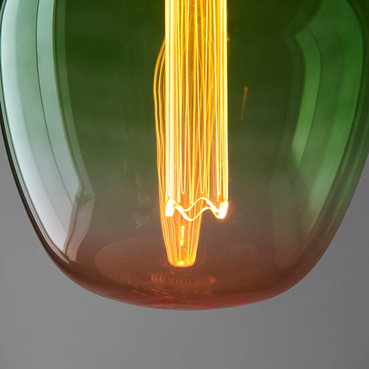 Close-up of Endon 2.8W E27 LED filament bulb with green-to-pink ombre glass, glowing warm white at 1800K over an etched acrylic diffuser sleeve.