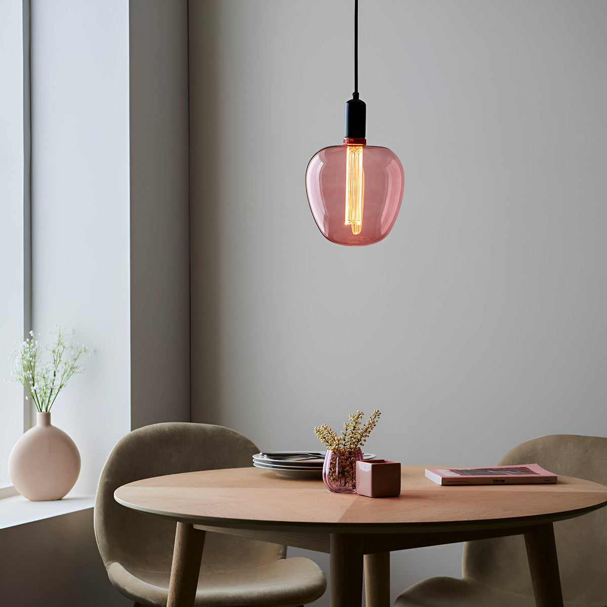 Pink-tinted E27 LED filament bulb glowing warm white in a black pendant fitting above a wooden dining table.
