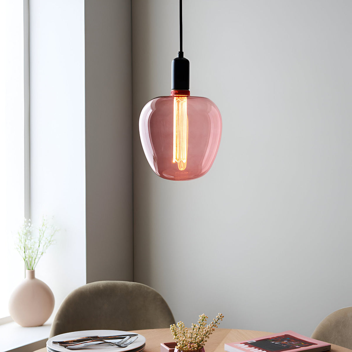 Pink-tinted E27 LED filament bulb glowing warm white inside a pink glass pendant light shade, in a dining room setting.