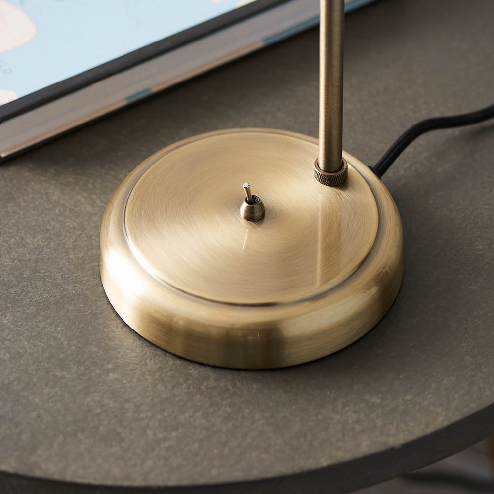 Close-up of the Brackley Table Lamp in Brass, showing the circular base with on/off toggle switch and knurled pole fitting on a stone surface.