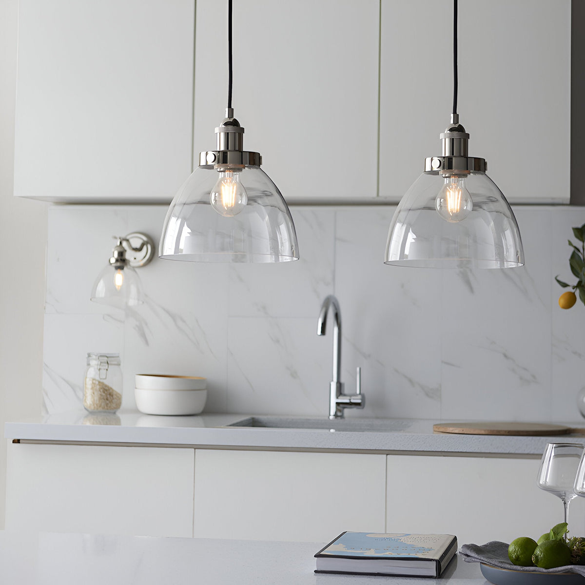 Endon Wentworth nickel wall light with clear glass shade beside two matching pendant lights over a white marble kitchen sink area.