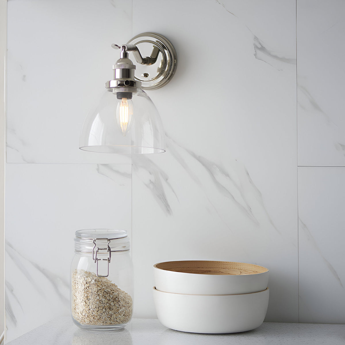 Endon Wentworth adjustable wall light in nickel with clear glass bell shade and E14 filament bulb, mounted on a marble wall above a jar and bowls.