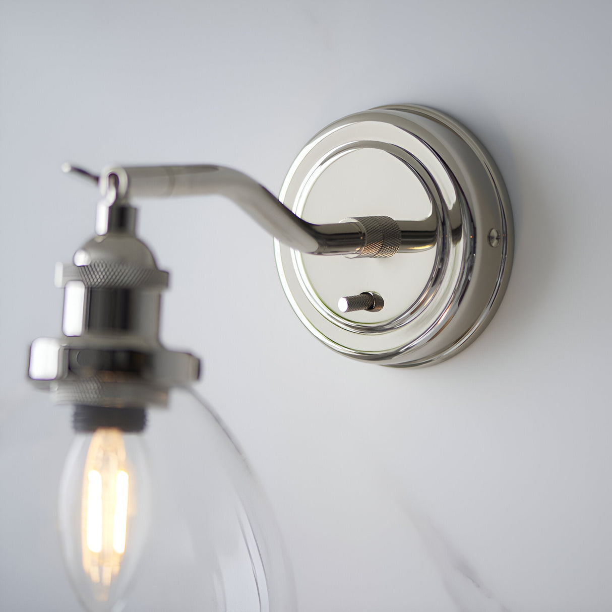 Close-up of the Endon Wentworth wall light in nickel, showing the round backplate with toggle switch, knurled arm and clear glass shade with lit E14 bulb.