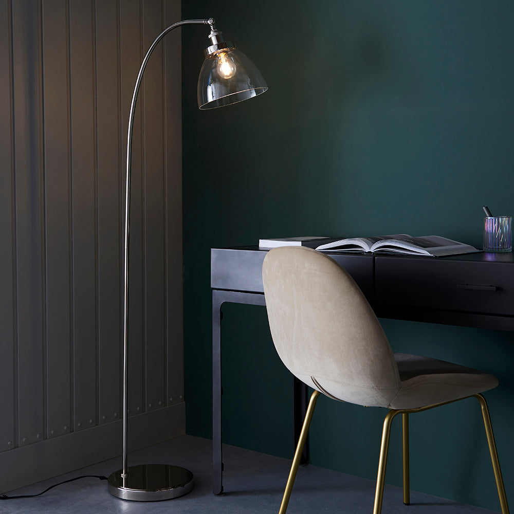Endon Wentworth nickel floor lamp with arched stem and clear glass shade, beside a dark desk and velvet chair in a green-walled study.