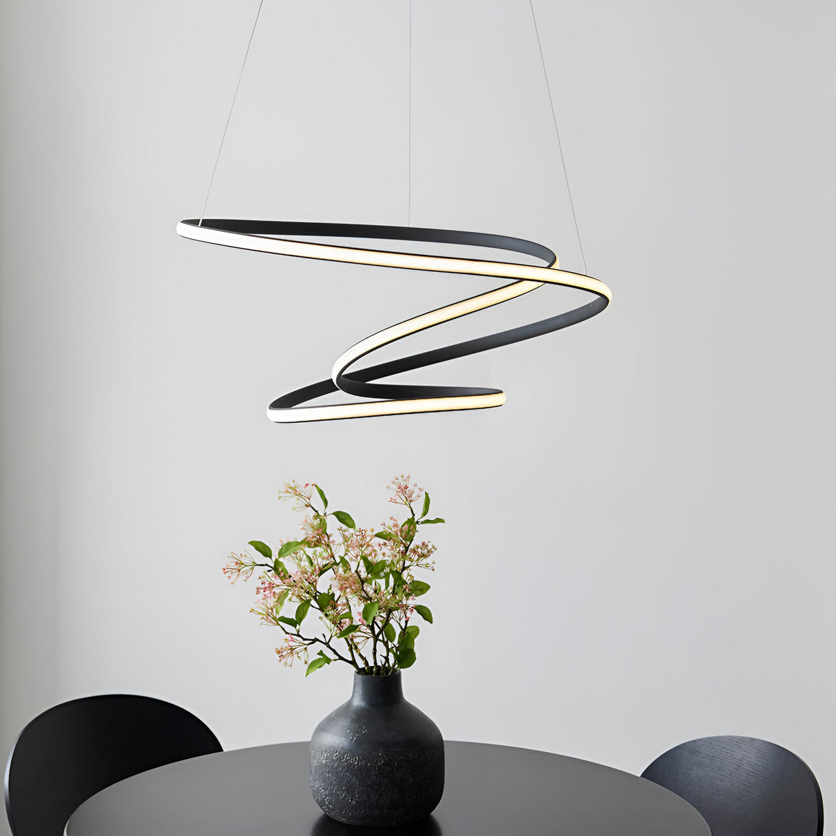 Endon Halden pendant light with a sculptural looped black frame and illuminated diffuser, suspended above a dining table with a black vase of flowers.