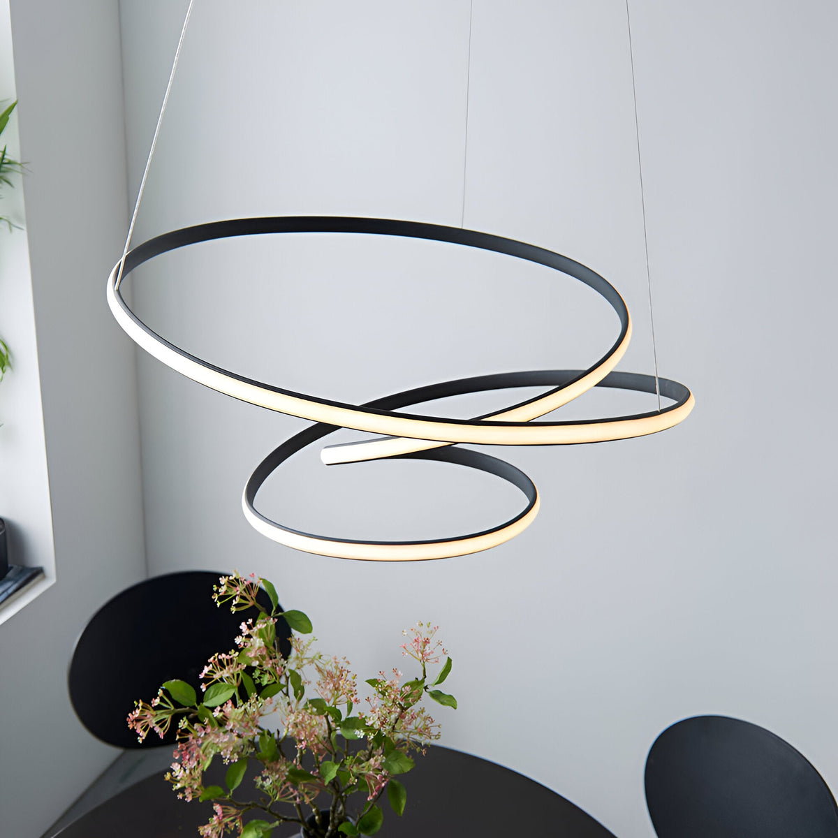 Endon Halden pendant light with sculptural looped LED rings in textured black and white diffuser, suspended above a black dining table with floral arrangement.