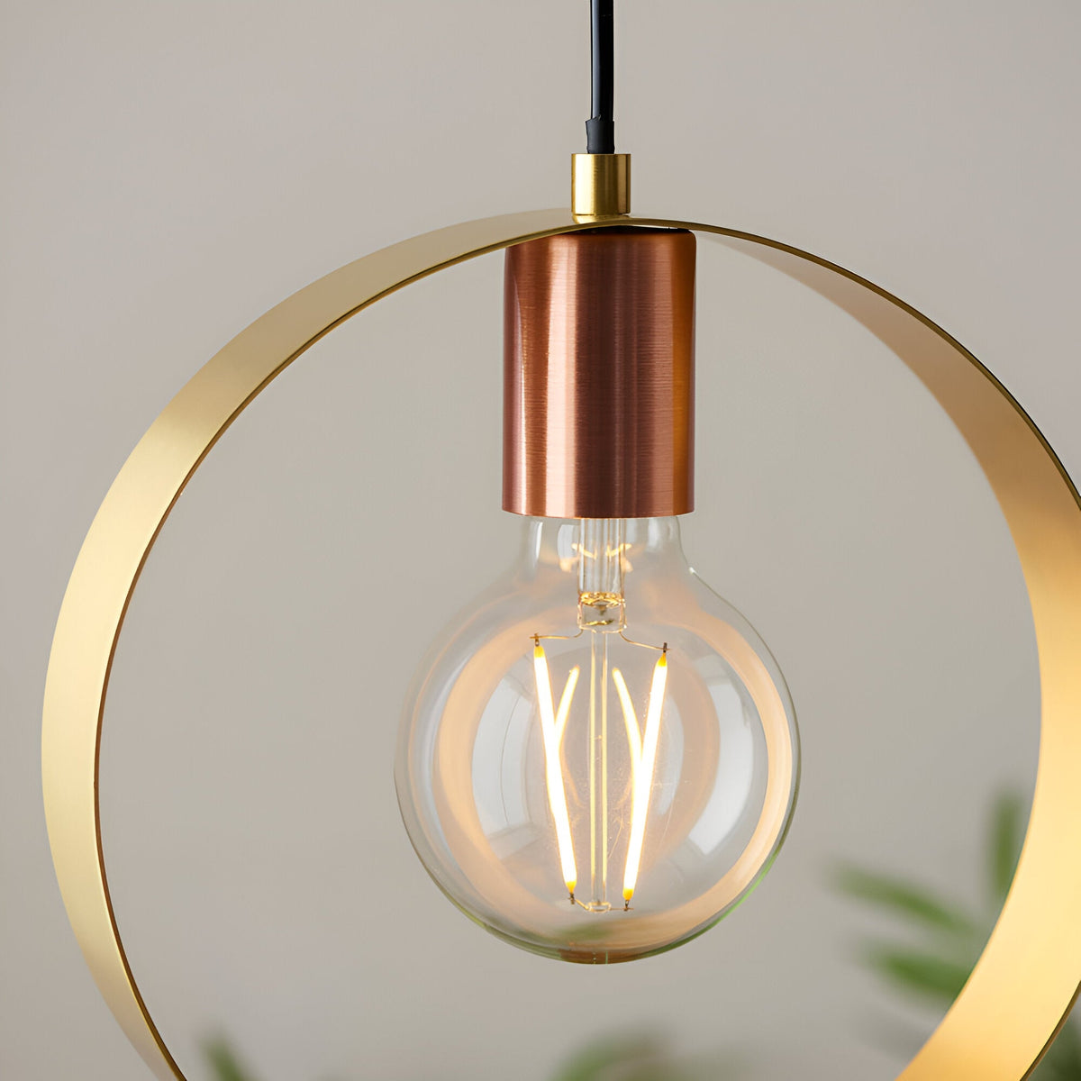 Brenmere pendant light with a round brass hoop frame and brushed copper lamp holder, holding an exposed E27 filament bulb, on a plain light background.