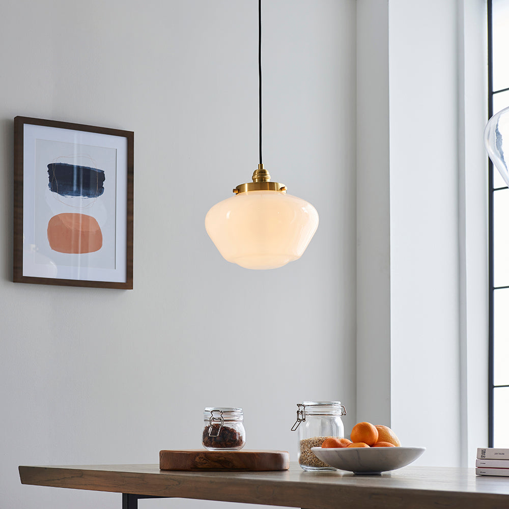 Endon Kedleston pendant light with brass fitting and rounded opal glass schoolhouse shade, hung above a wooden dining table in a bright kitchen setting.
