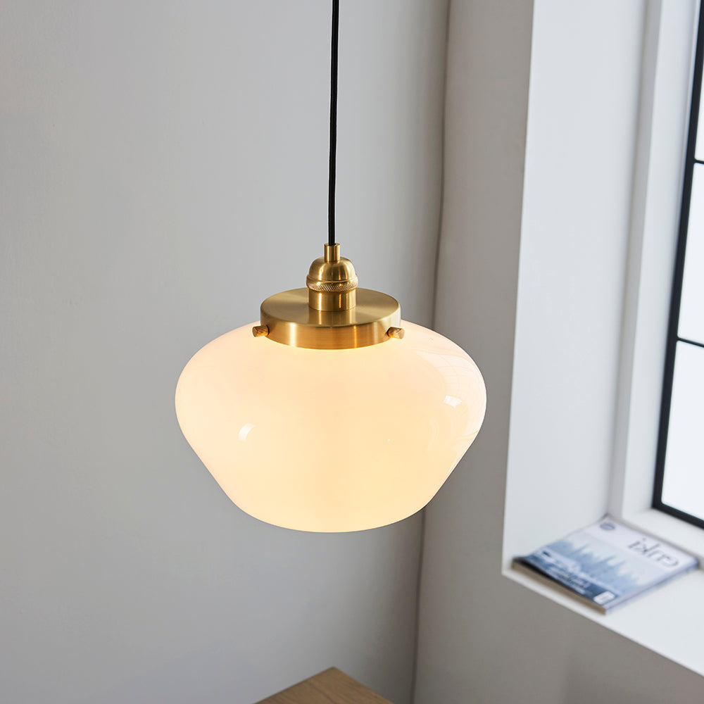 Endon Kedleston pendant light with a rounded opal glass shade and brass fitting on a black flex, hanging beside a window against a light grey wall.