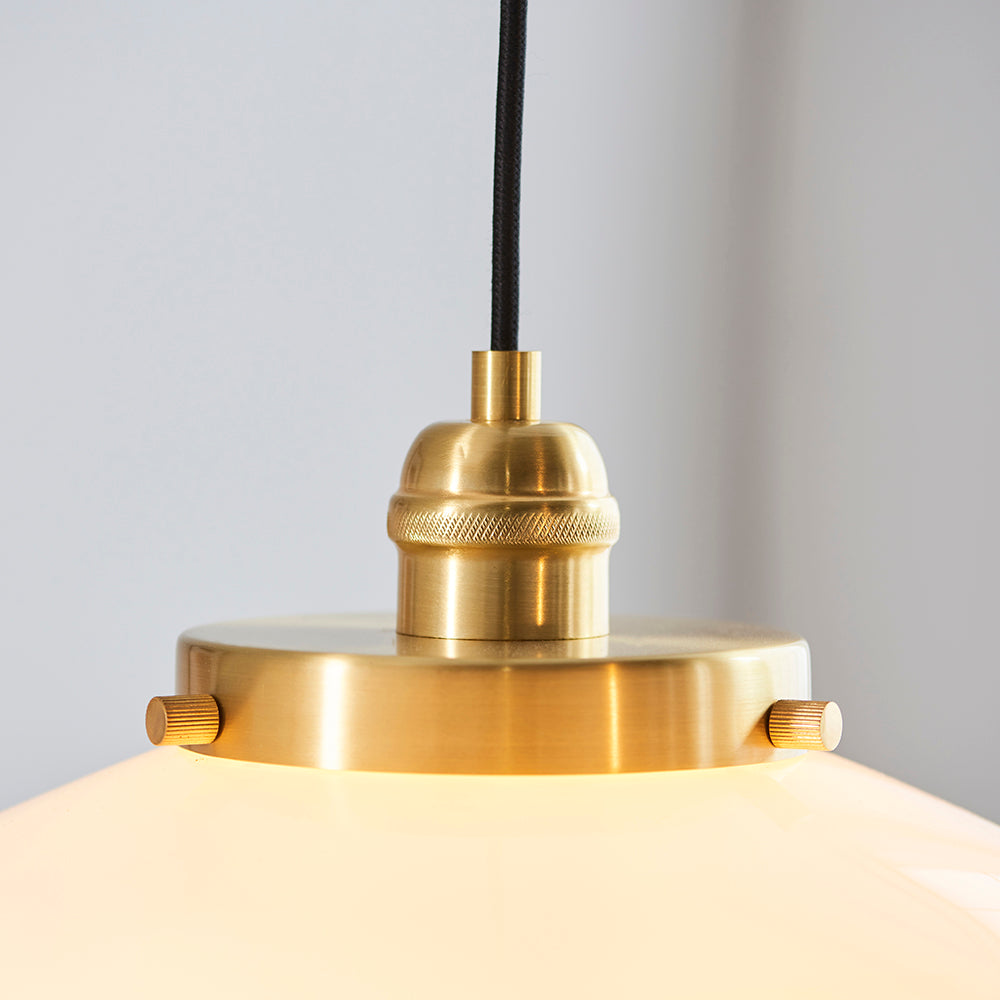 Close-up of the Endon Kedleston pendant light showing its brushed brass fitting, knurled collar, black fabric flex, and the top of the opal glass shade.