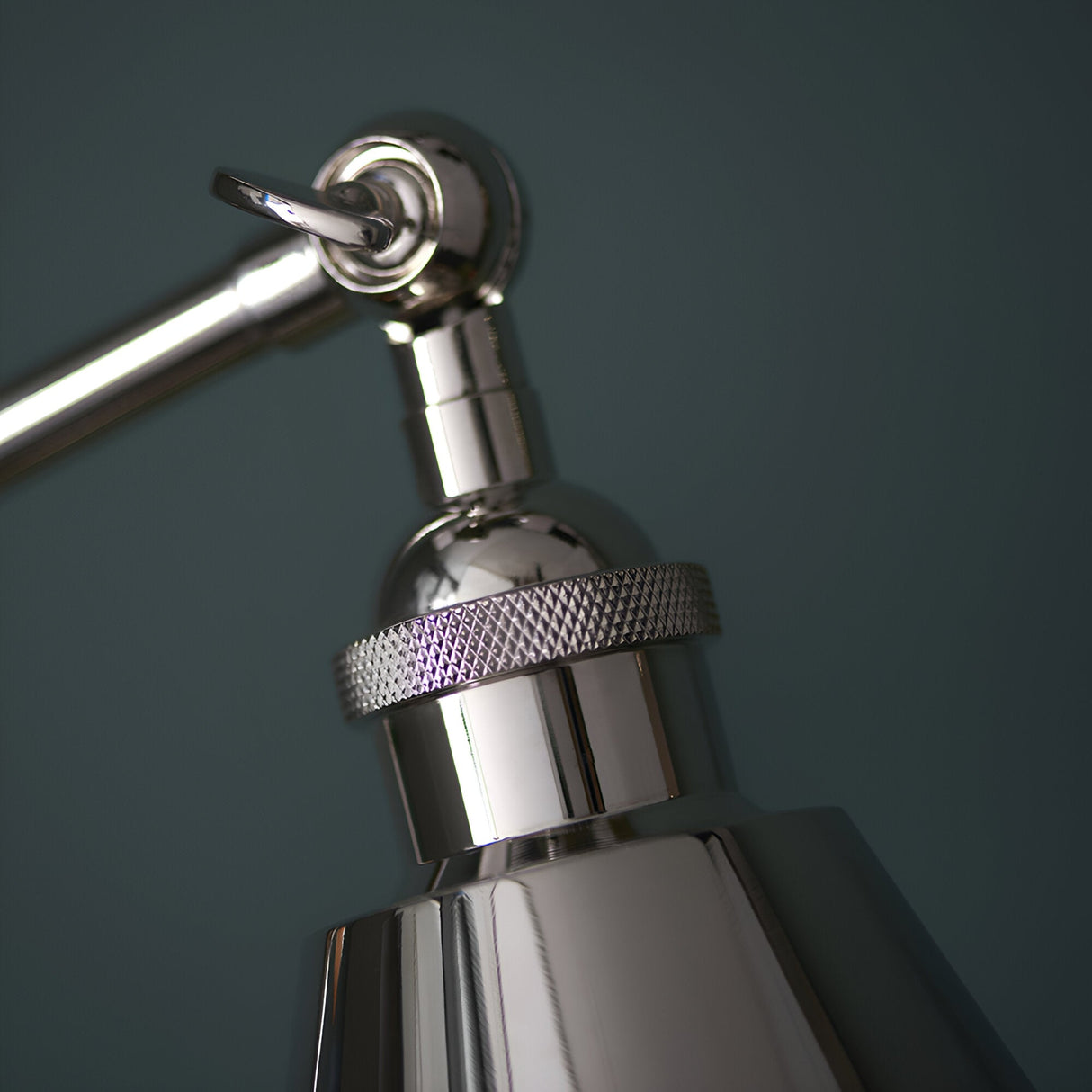 Close-up of Endon Brackley table lamp head in bright nickel, showing knurled ring detail, adjustable joint and toggle switch against a dark teal backdrop.