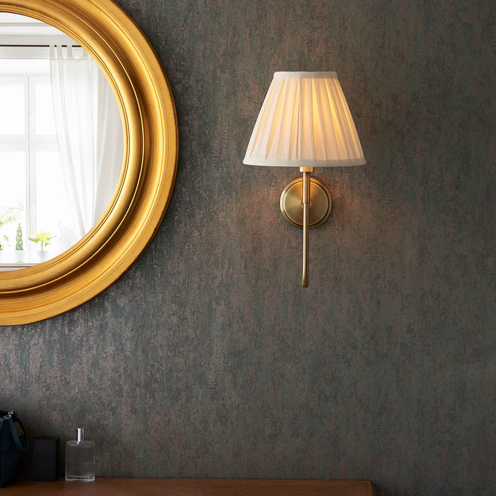 Endon Cliffdon antique brass wall light with a tapered pleated cream shade, mounted on a dark textured wall beside a round gold-framed mirror.