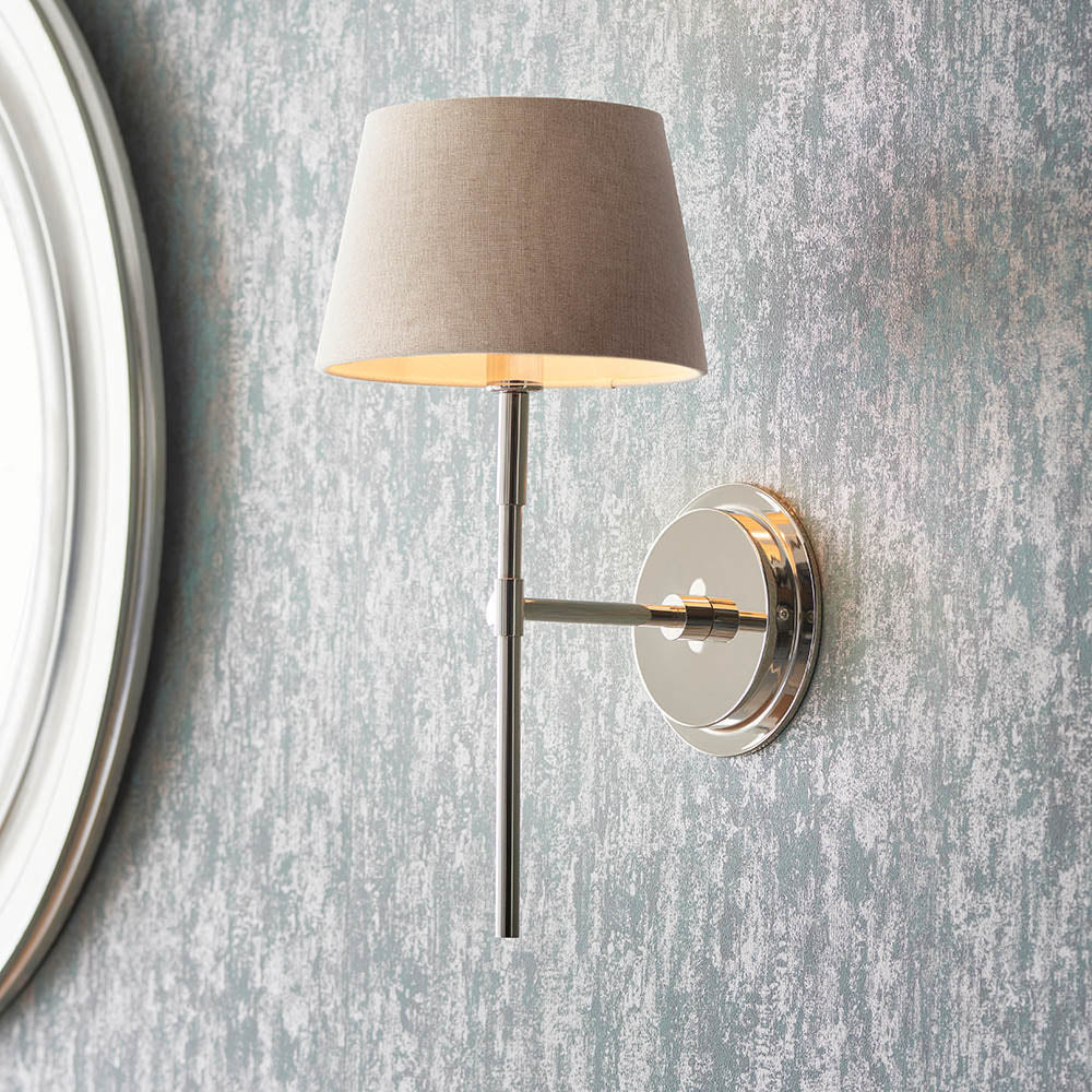 Endon Chartwell nickel wall light with slim upright bracket and tapered grey fabric shade, mounted beside a white-framed round mirror on a grey wall.
