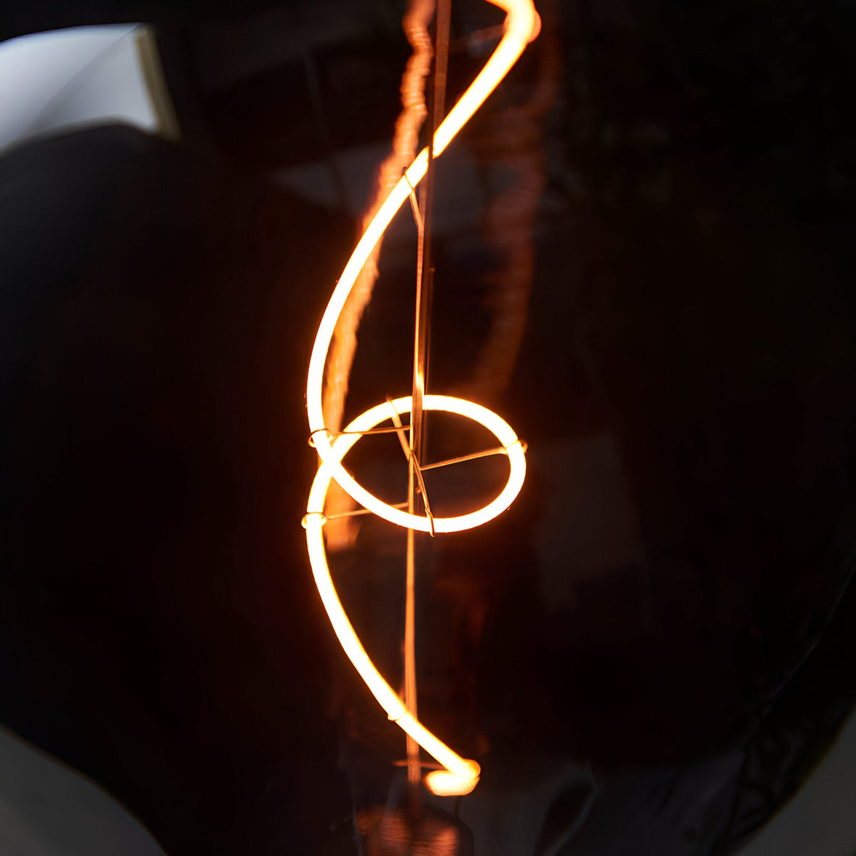4W E27 LED Filament Wisp Bulb in smoke glass, showing a swirling wisp-shaped filament glowing warm white against a dark background.