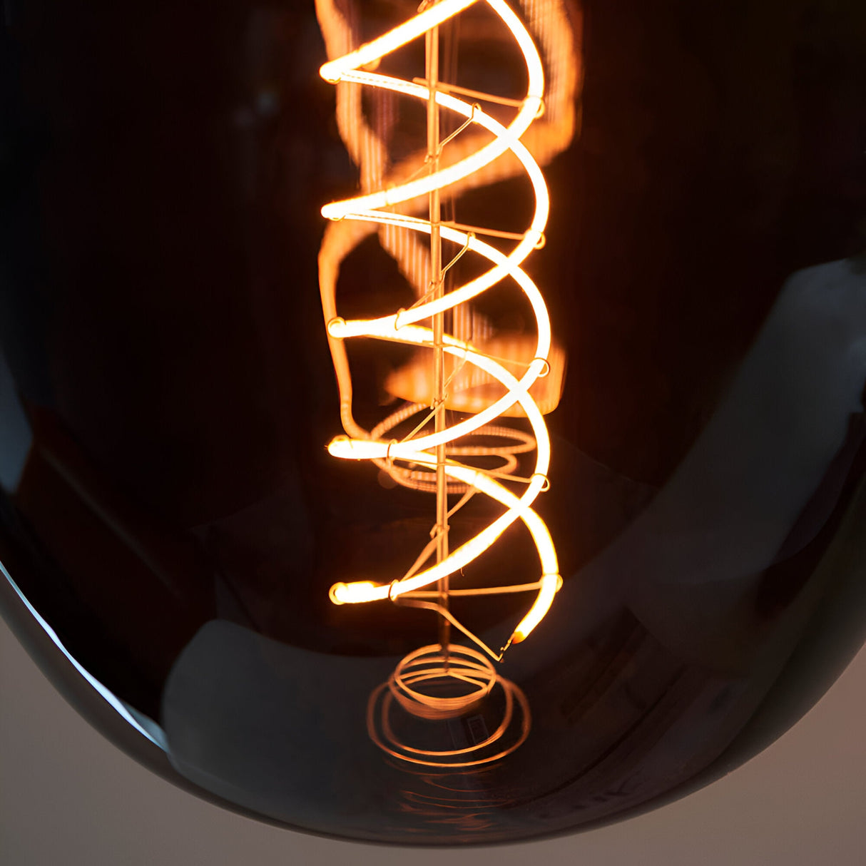 Close-up of Endon 4W E27 LED filament helix bulb showing the illuminated double-helix filament glowing warm amber through smoked glass.