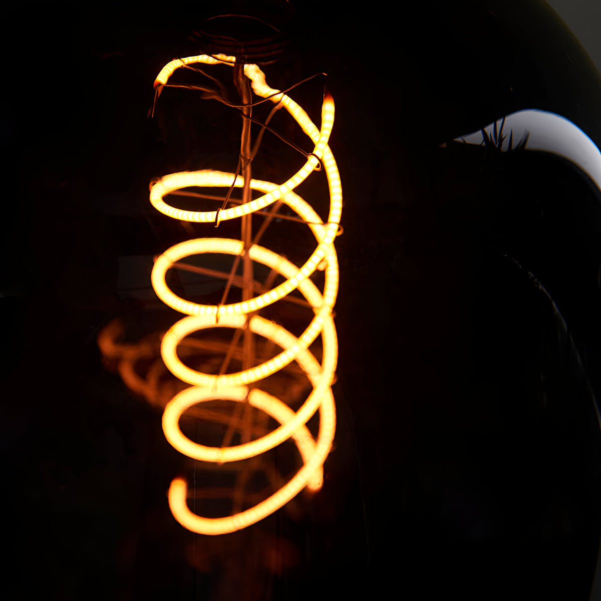 Endon 4W E27 LED filament bulb with glowing amber double-helix filament shown in close-up through smoked glass against a dark background.
