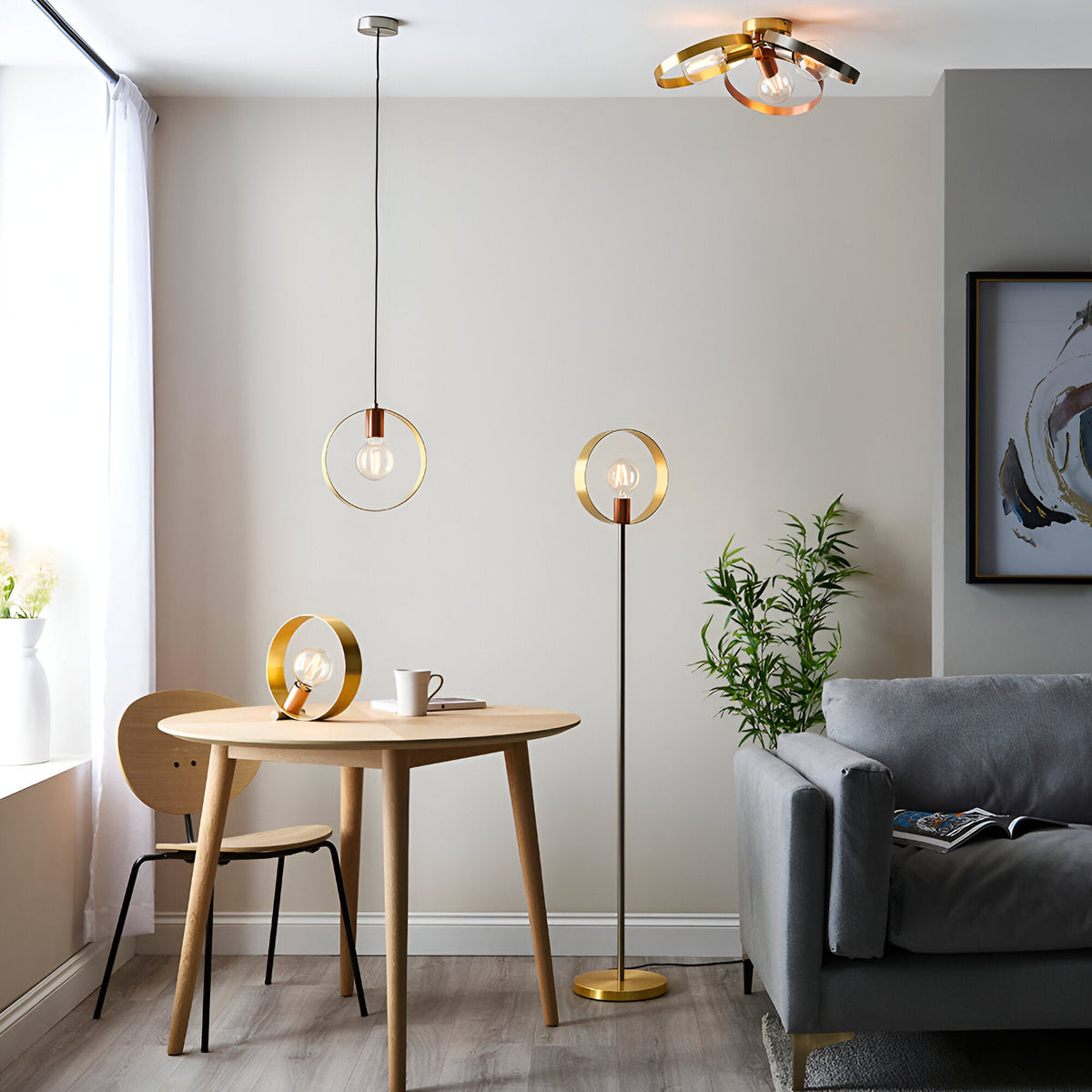 Brenmere Floor Lamp with brass, copper and nickel open hoop frame and exposed bulb, shown beside a dining table in a living room.