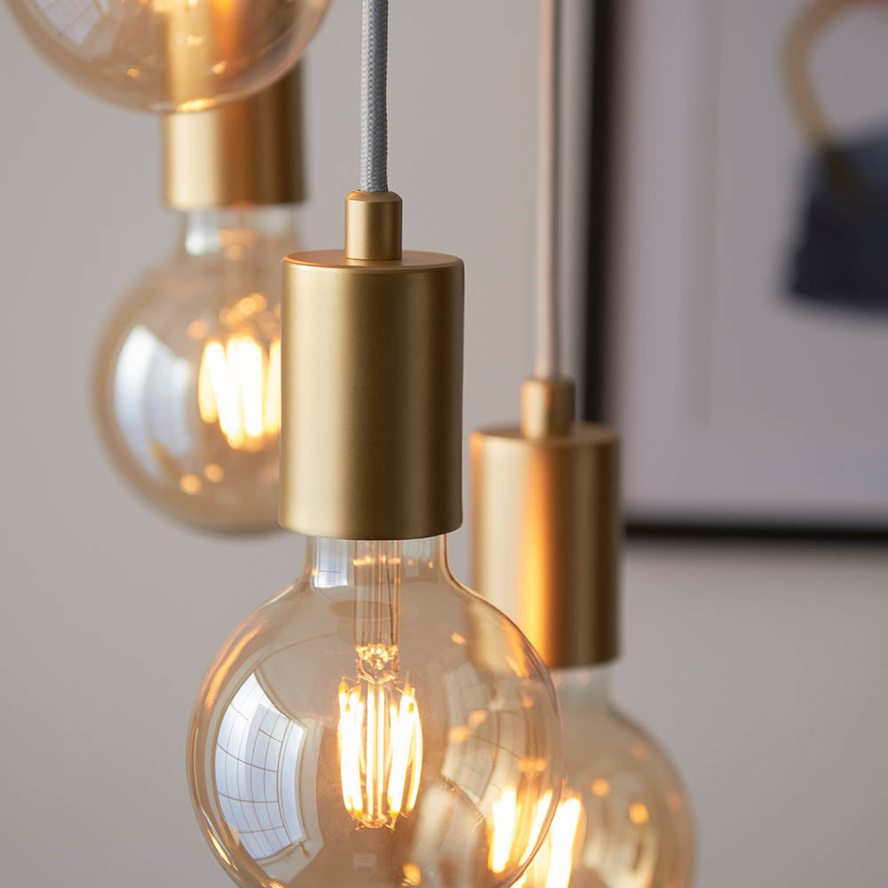 Marlowe 6 Light Pendant in gold, close-up of globe bulbs in matte gold holders on grey fabric flex, industrial-modern style.