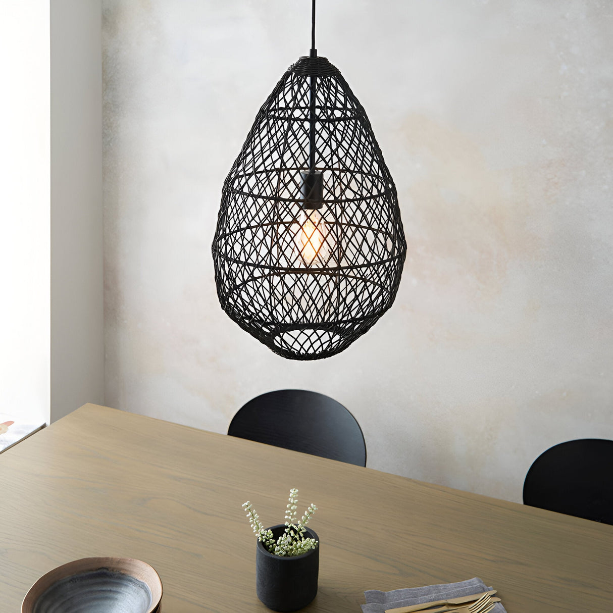 Endon Chartdale pendant light in black woven rattan with a teardrop open-weave shade and E27 bulb, hanging above a wooden dining table.