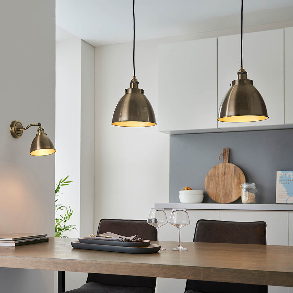 Endon Bramdale brass wall light with adjustable knuckle and dome shade, shown beside two matching pendant lights above a kitchen dining table.