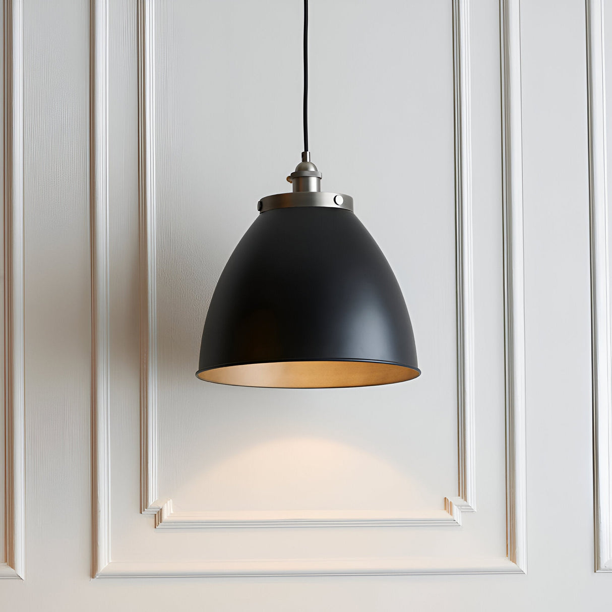 Endon Bramdale medium pendant light with matt black rolled-edge metal shade, aged pewter detailing and inner, on black flex against white panelled wall.