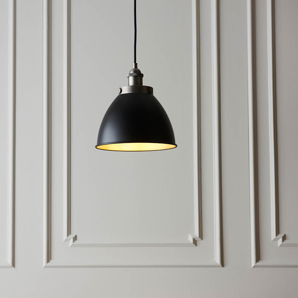 Endon Bramdale Small Pendant in matt black with rolled-edge metal shade, aged pewter detailing and inner, hung on black flex against panelled grey wall.